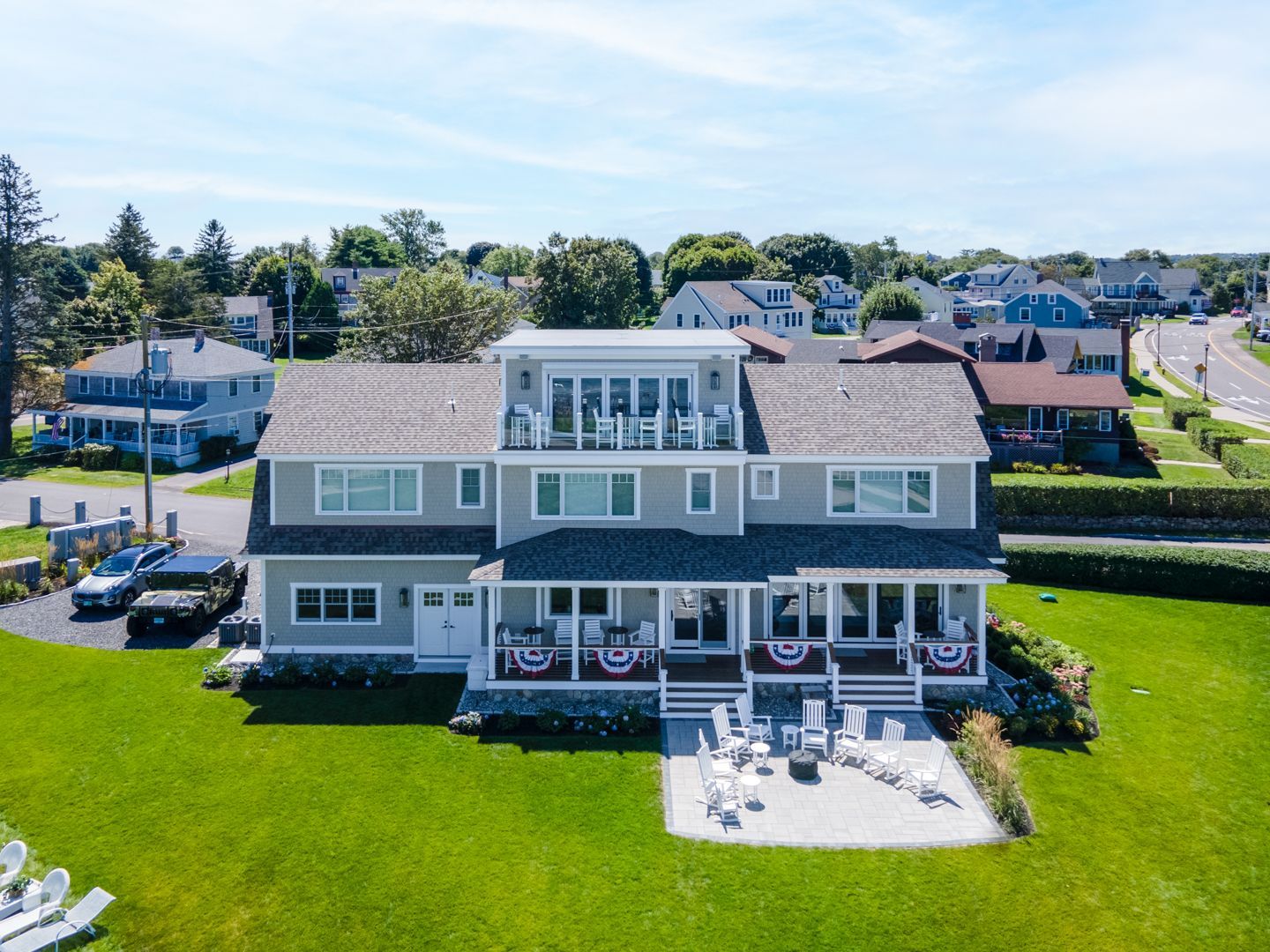 Large gray house with a backyard patio, deck chairs, and a green lawn under a blue sky