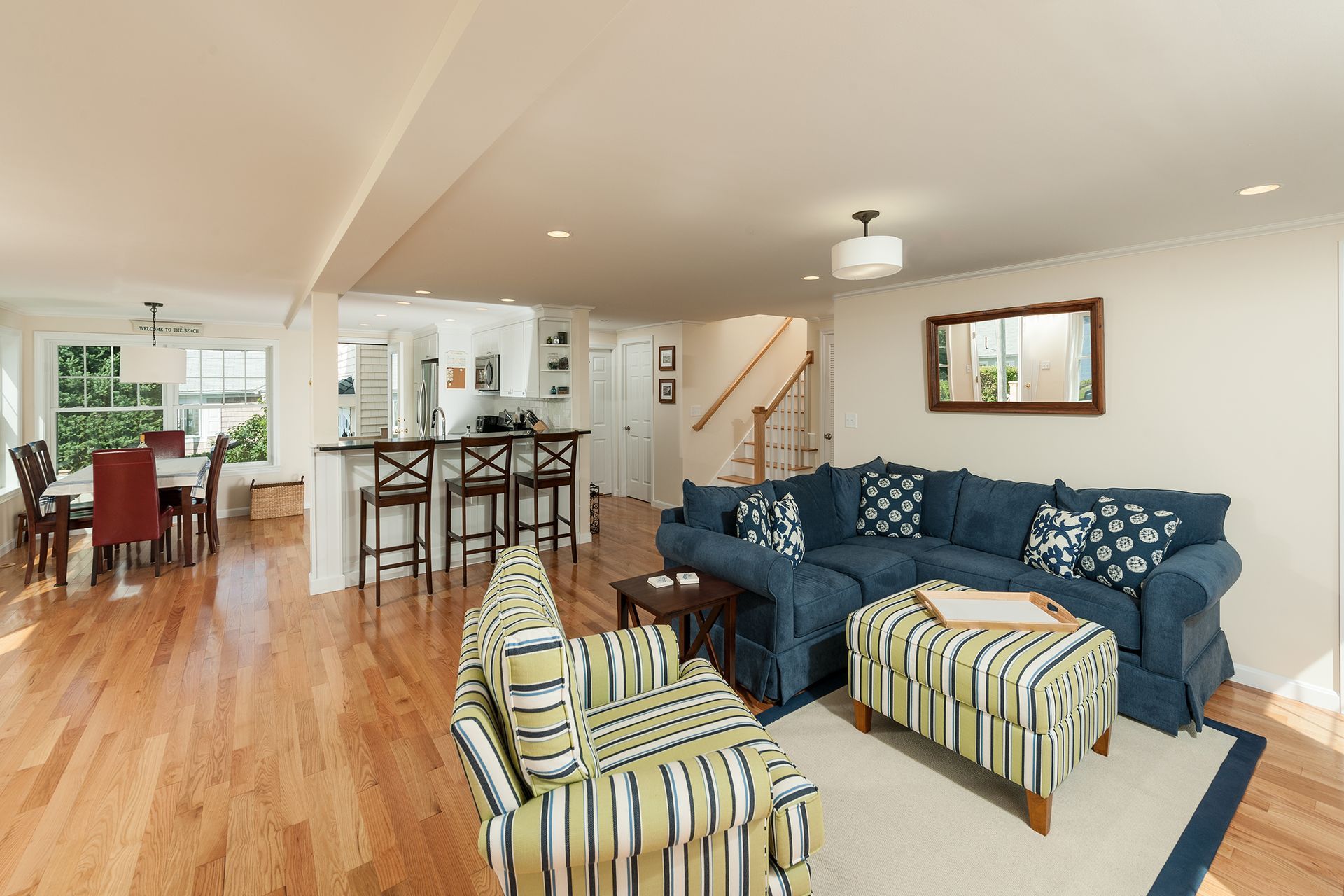 Open-concept living room with blue sofa, striped chairs, kitchen island, and hardwood floors