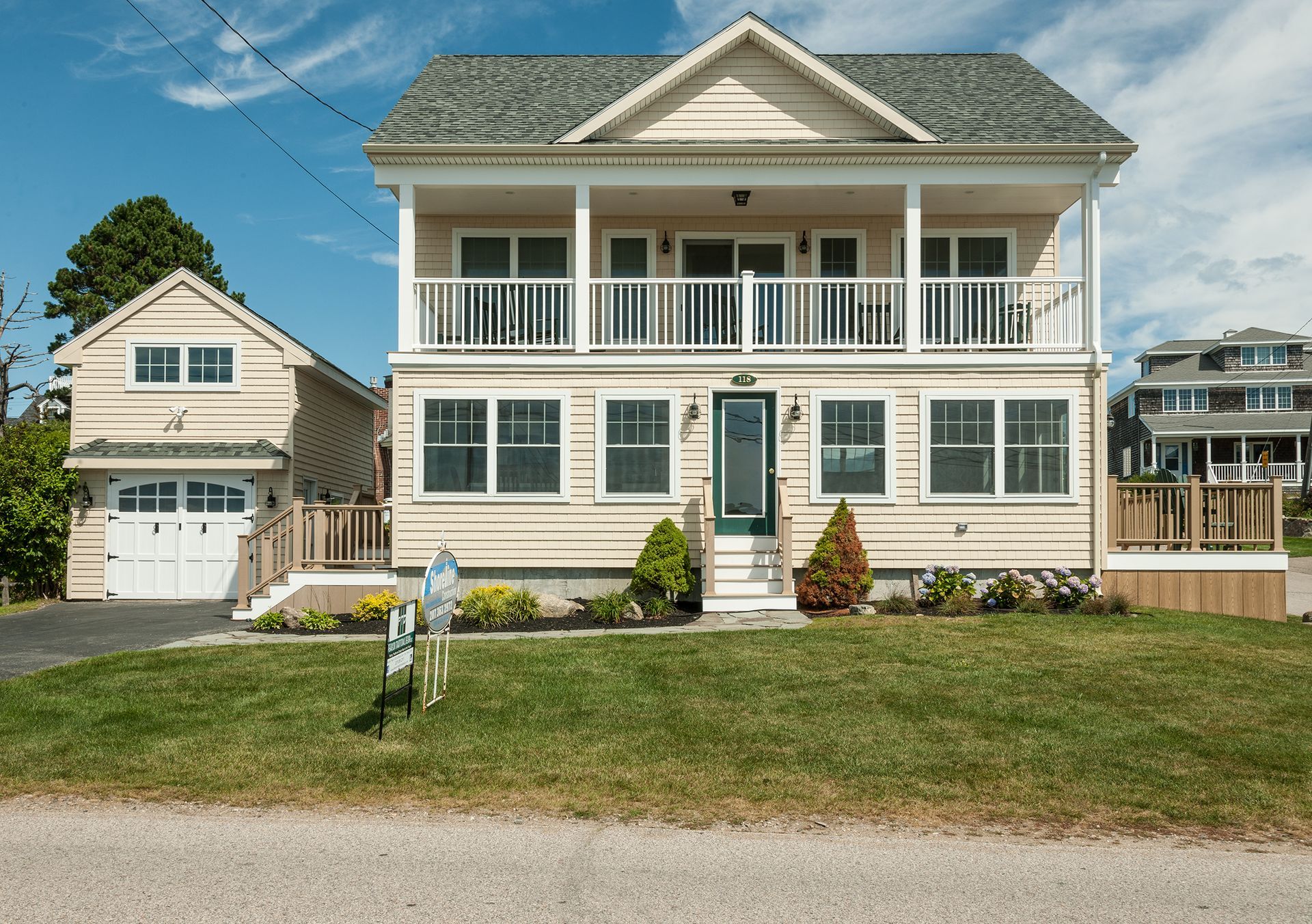 Two-story white house with porch and garage in a grassy suburban neighborhood under a blue sky