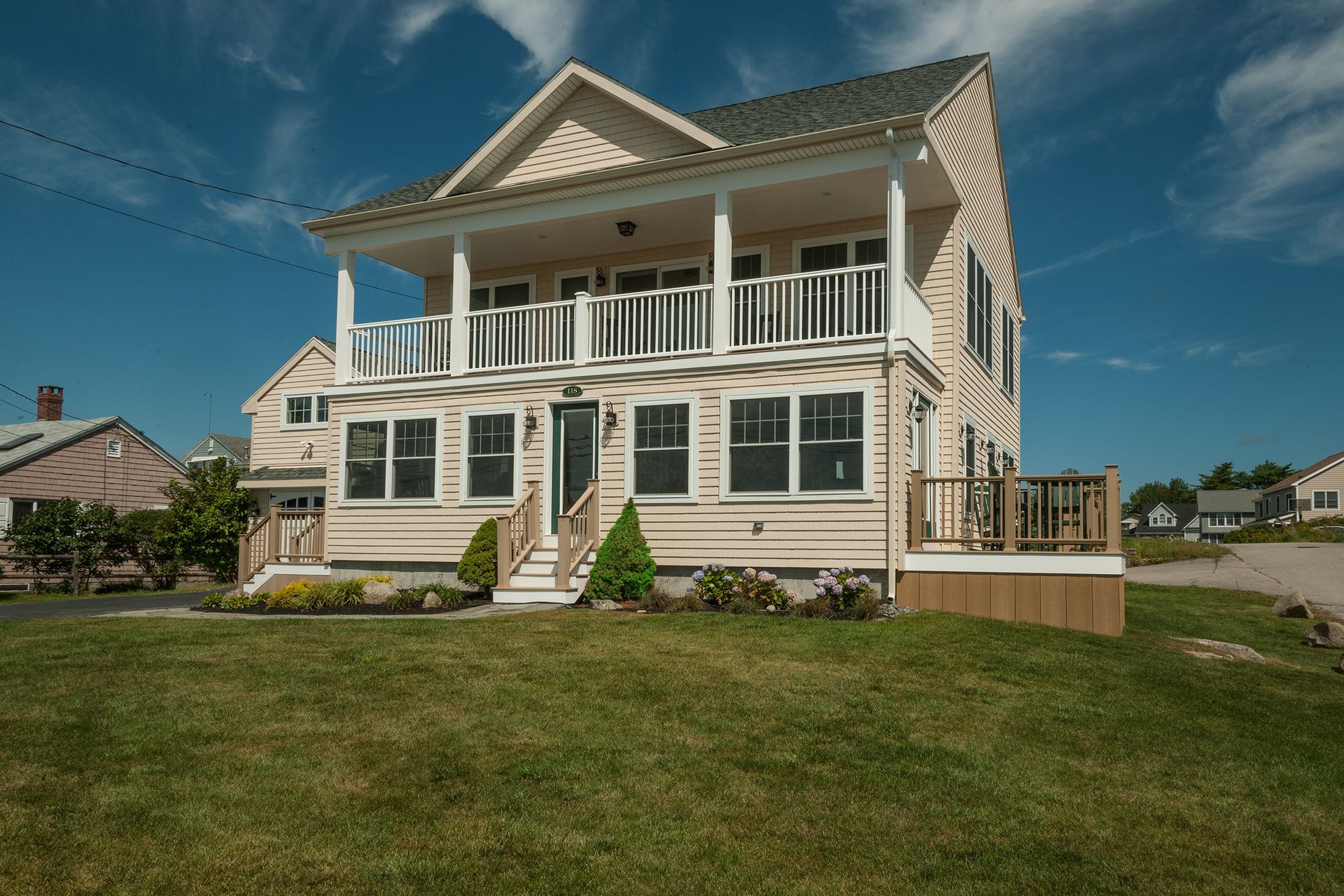 Large cream-colored seaside house with wraparound porch and green shutters under a blue sky