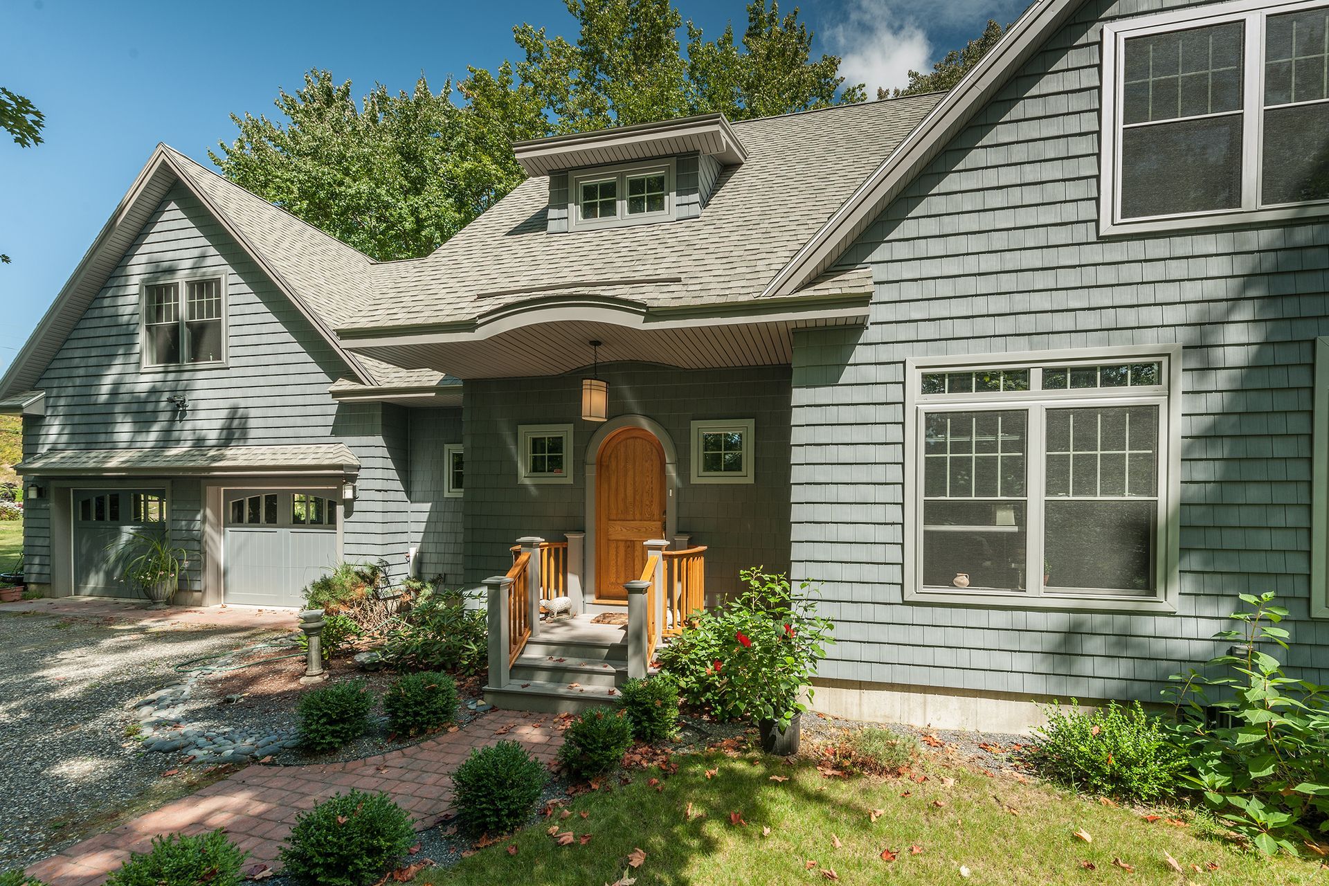 Gray house with a curved roof, front porch, and orange door surrounded by green garden plants