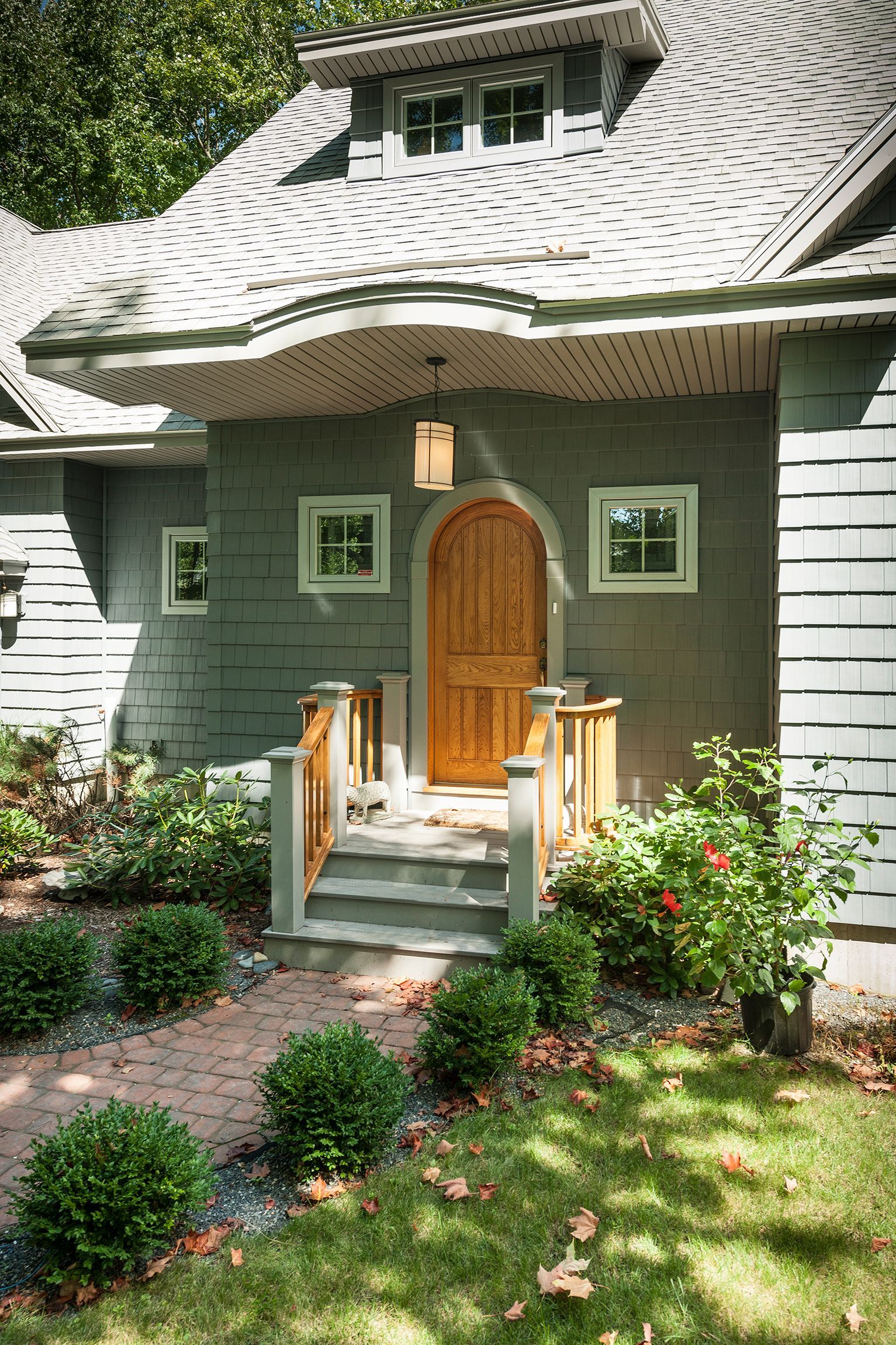 Quaint green cottage entrance with curved shingled roof, wooden door, and small front garden