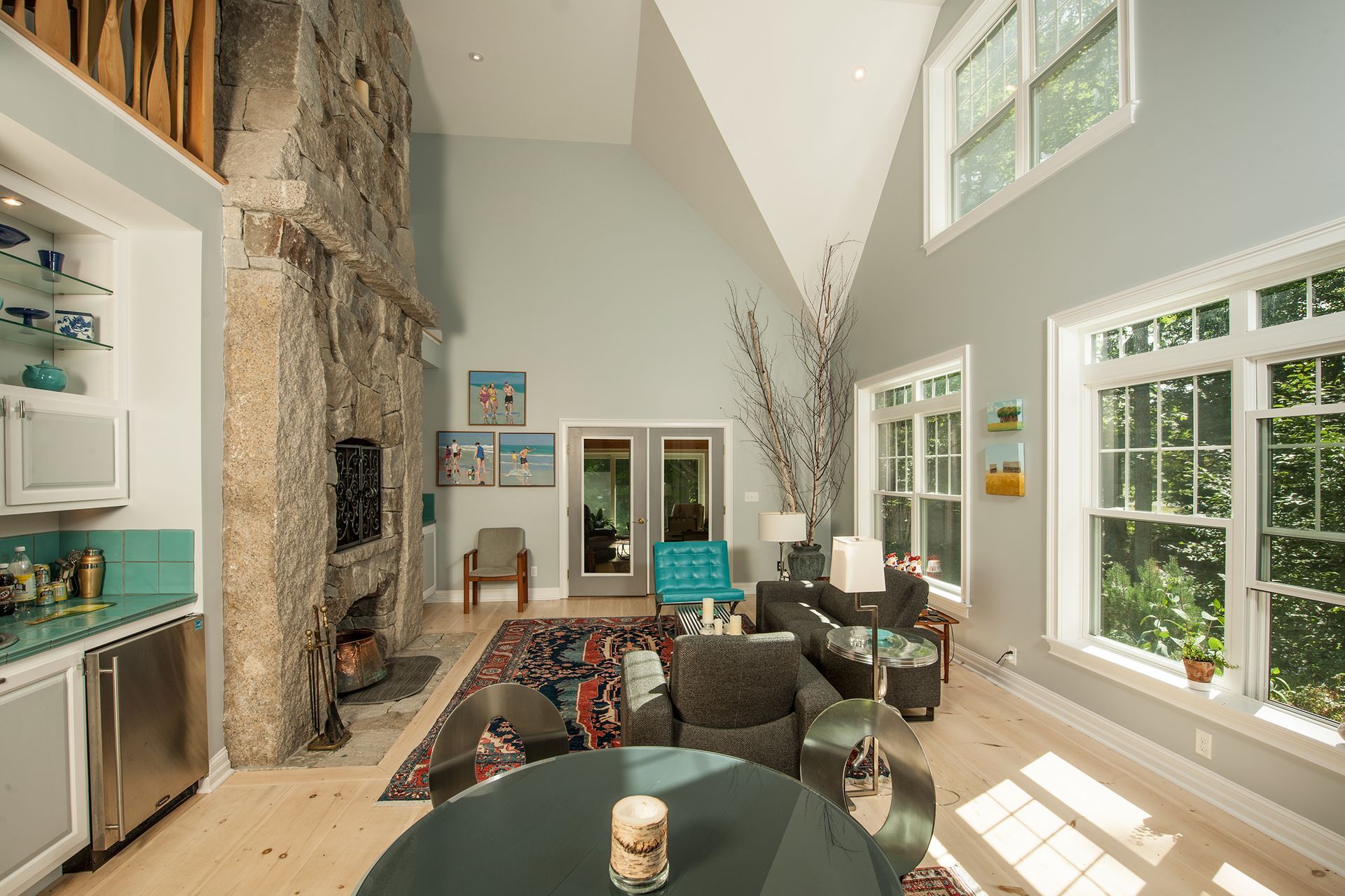 Bright living room with stone fireplace, high windows, and teal-accented seating on a rug