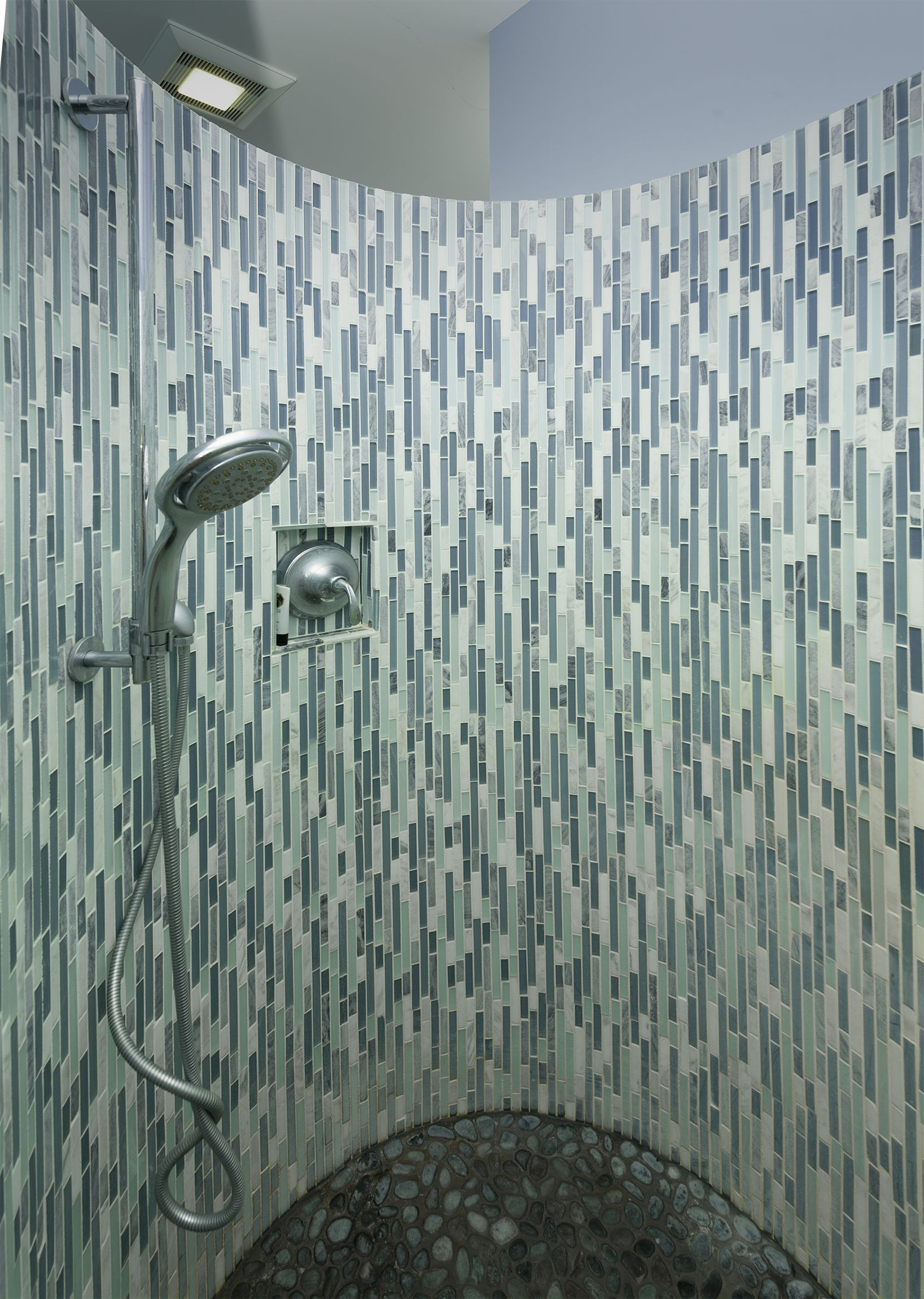 Curved tiled shower stall with chrome shower fixtures and mosaic floor drain
