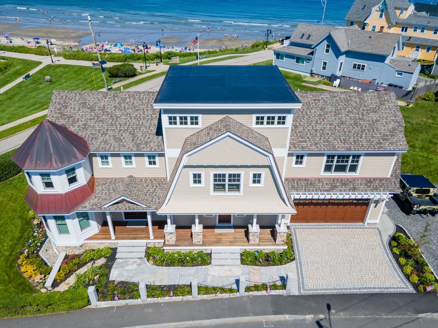 Aerial view of a large beige beach house with a blue roof near the shoreline and ocean.