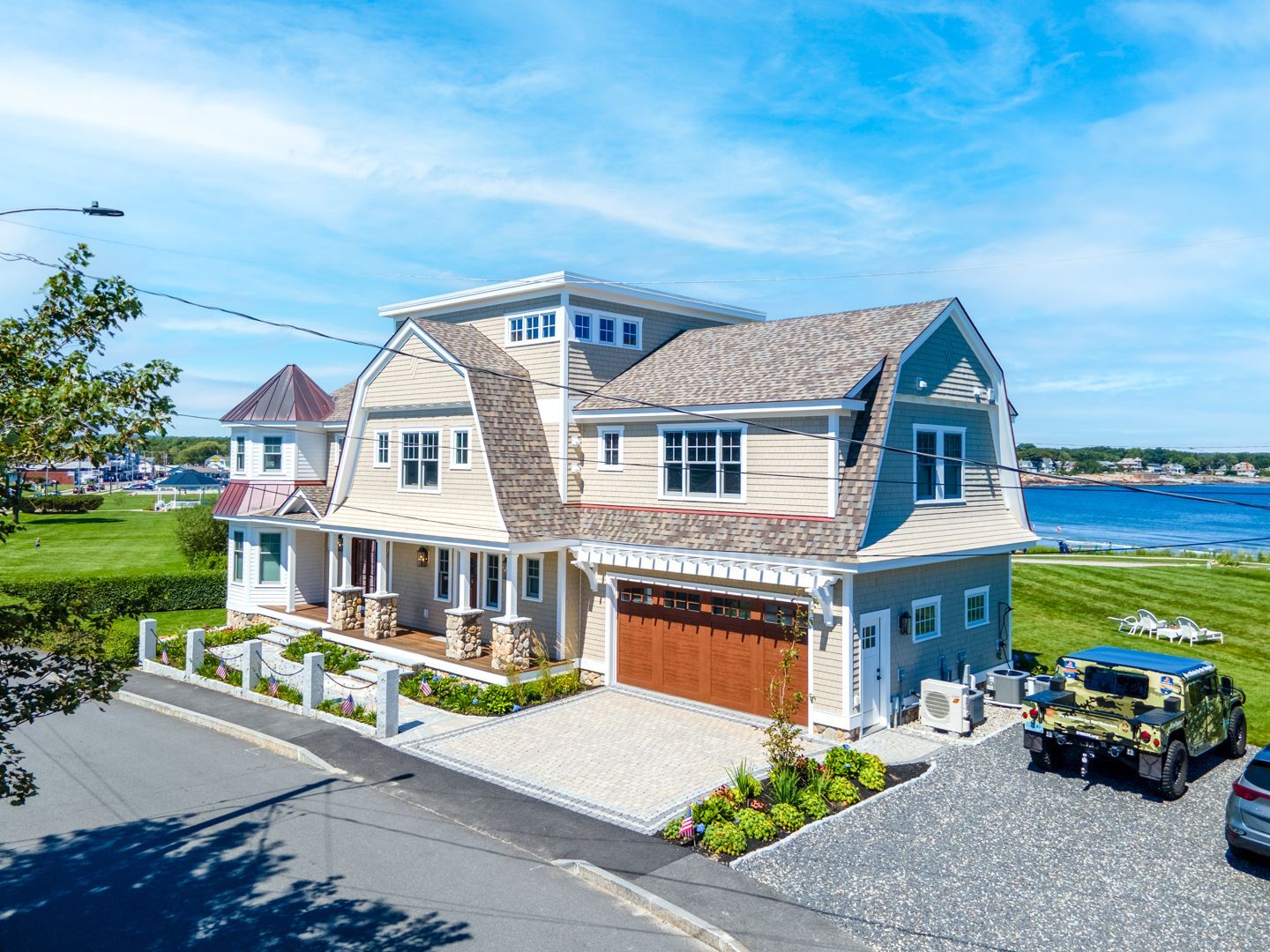 Large blue coastal house with white trim, driveway, and ocean view under a bright sky