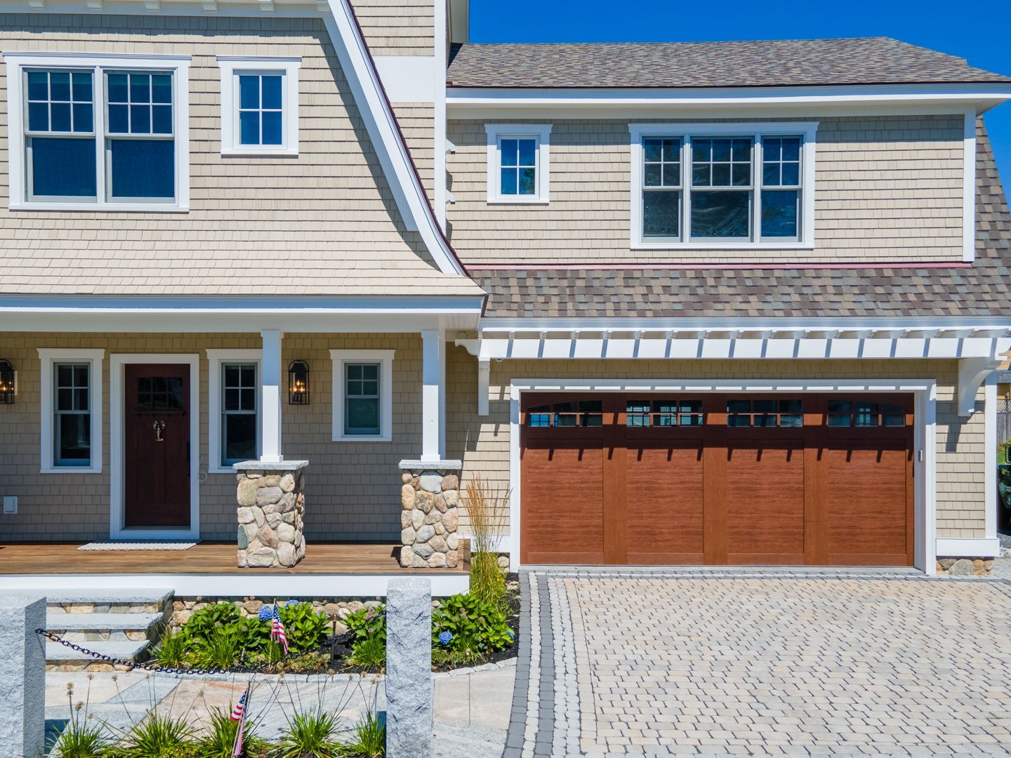 Suburban house exterior with beige siding, stone accents, and double garage with wooden doors