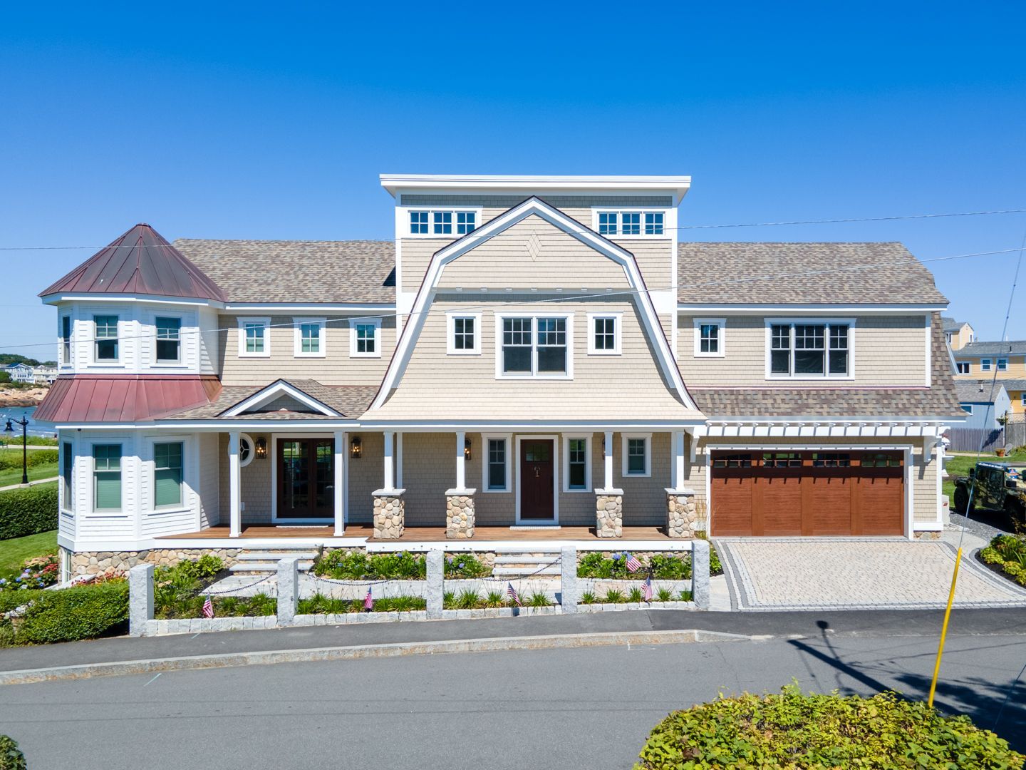 Large coastal house with beige siding, white trim, and a red garage under a clear blue sky.