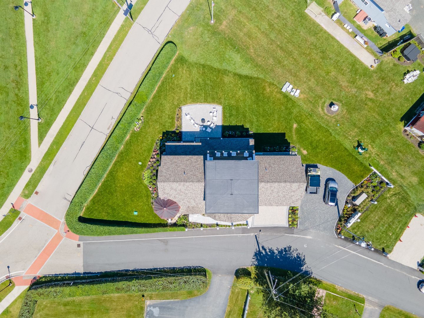 Aerial view of a house at a street corner with a driveway, lawn, and parked cars.