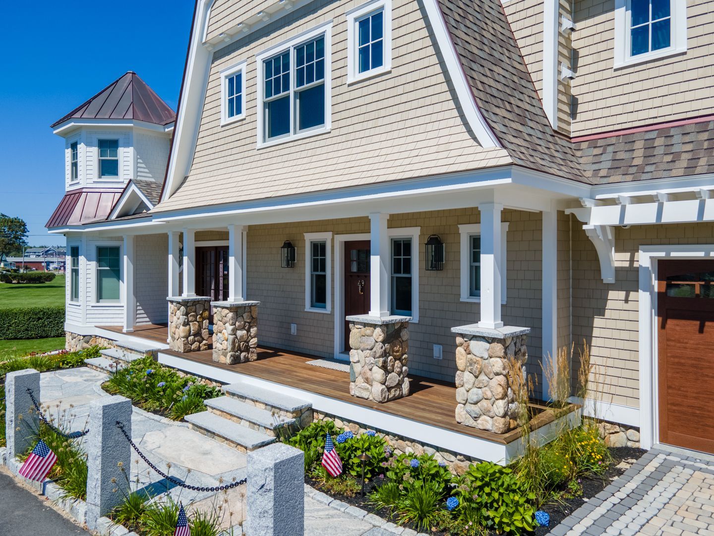 New beige house with porch, stone steps, and flower beds under a blue sky