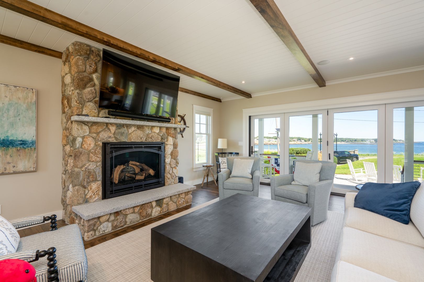 Bright living room with stone fireplace, gray sofas, and large windows overlooking water.