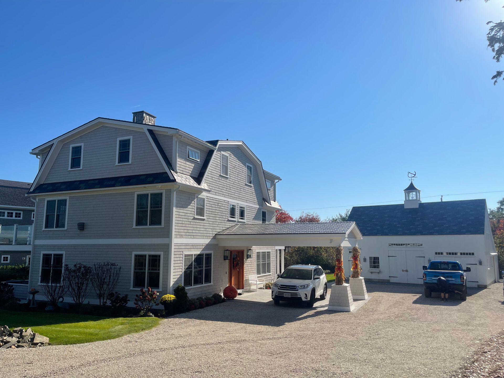 Large white house with attached carport and gravel driveway under a clear blue sky