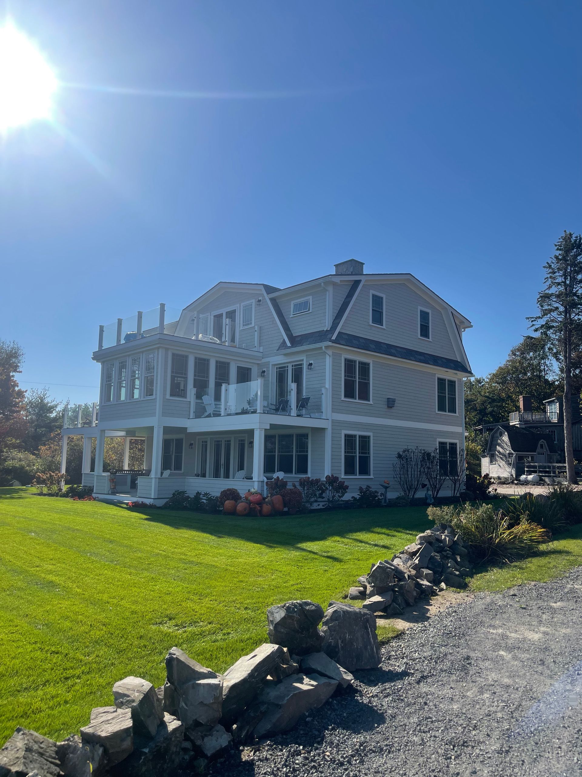 White Victorian-style house with porch on a sunny green lawn beside a gravel drive