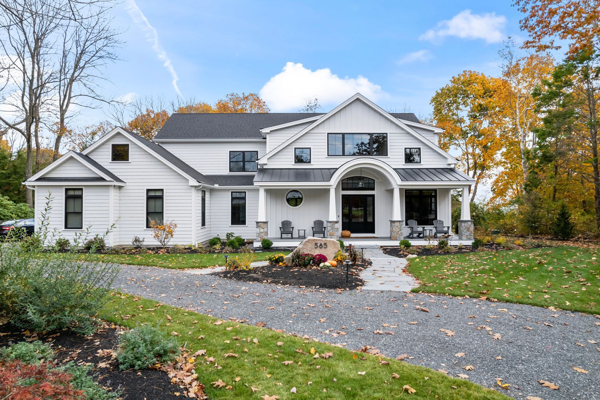 White farmhouse with a curved driveway, autumn trees, and a landscaped front yard
