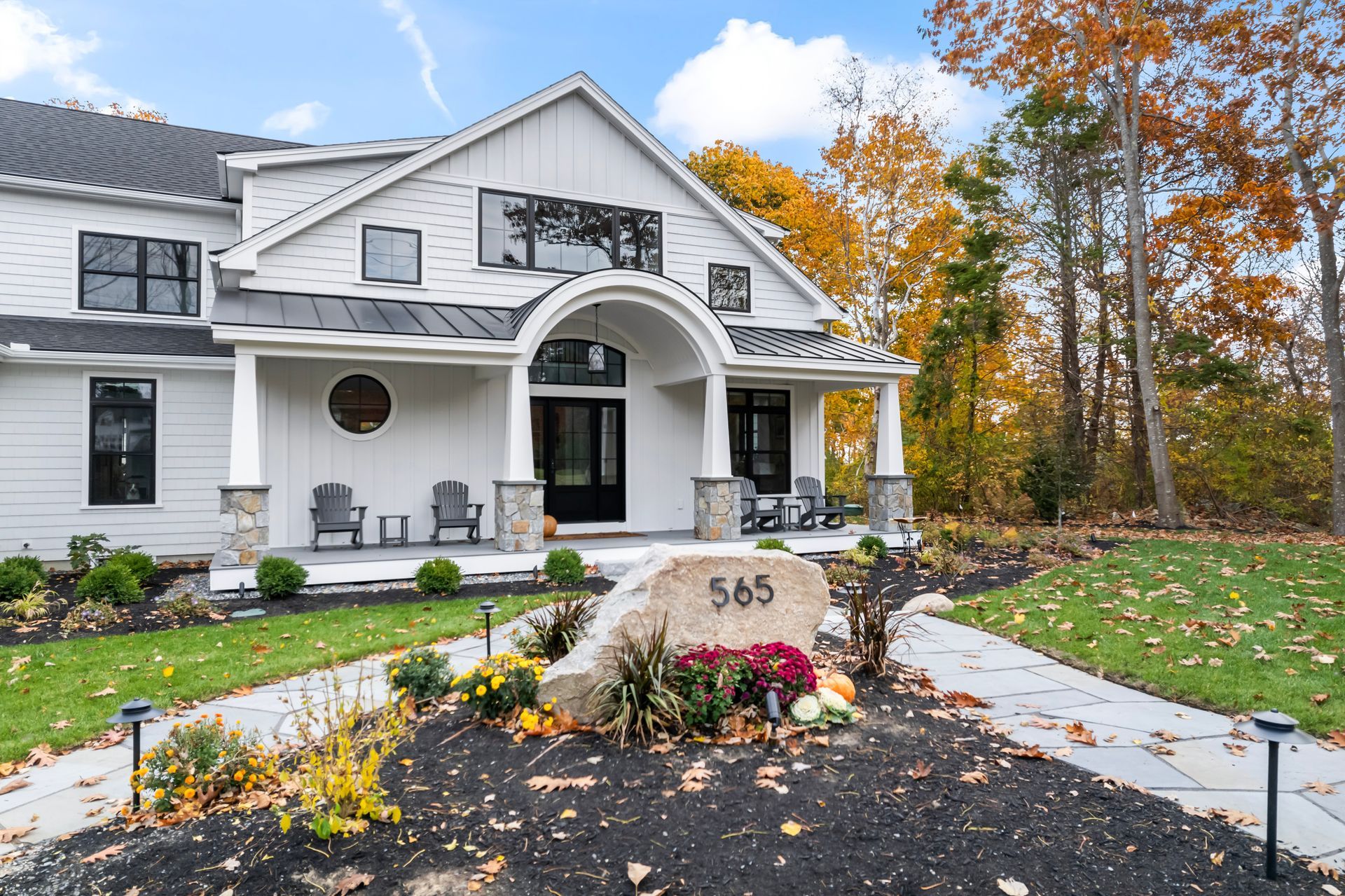 White two-story house with arched porch and autumn landscaping, number 565 on stone sign