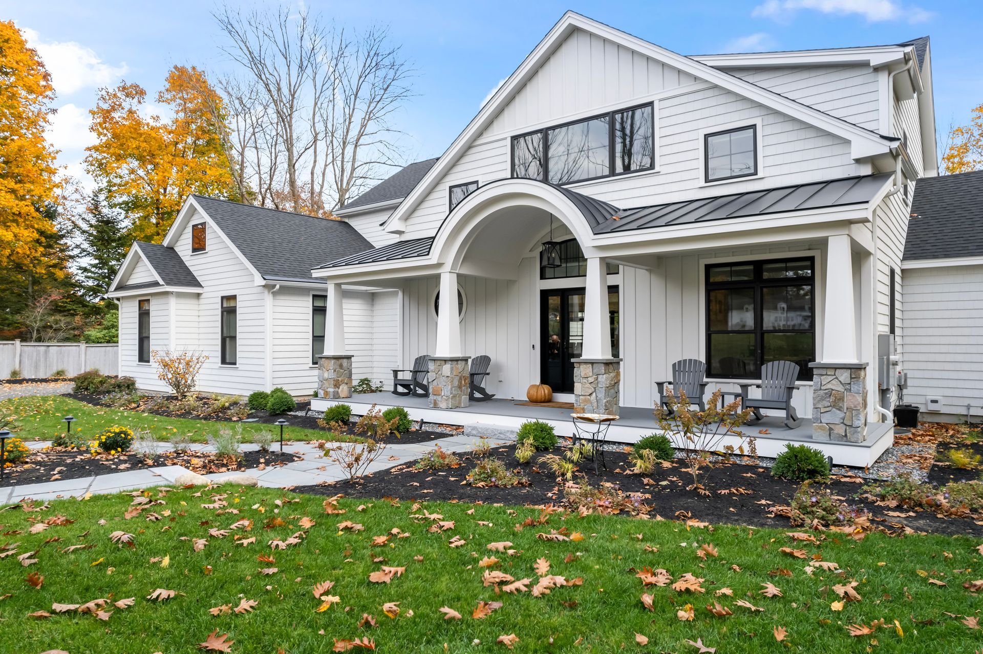 Large white suburban house with a covered front porch, stone walkway, and autumn landscaping