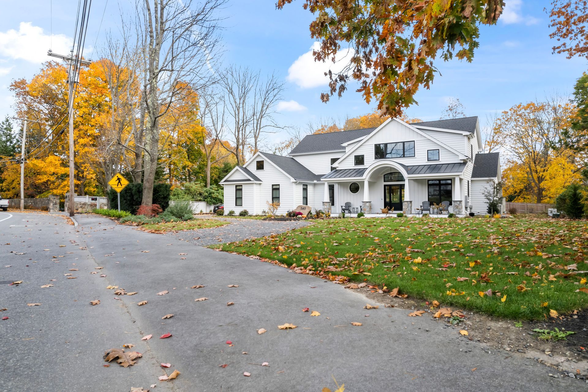 Suburban house with white siding on a curving street, surrounded by autumn trees and fallen leaves