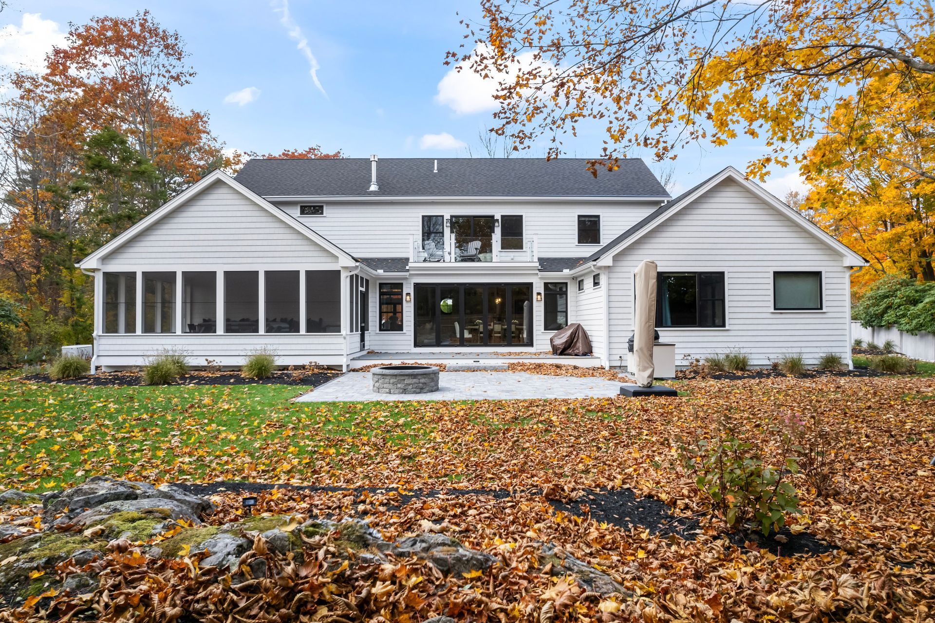 White house with large front porch, autumn trees, and fallen leaves in the yard