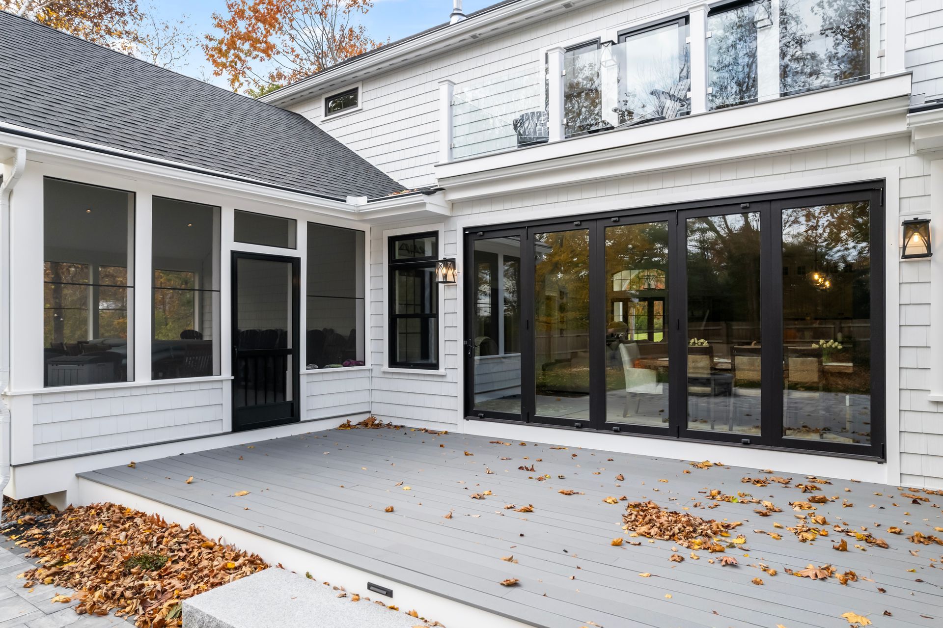 White house patio with large black-framed glass doors and fallen leaves on a light gray deck