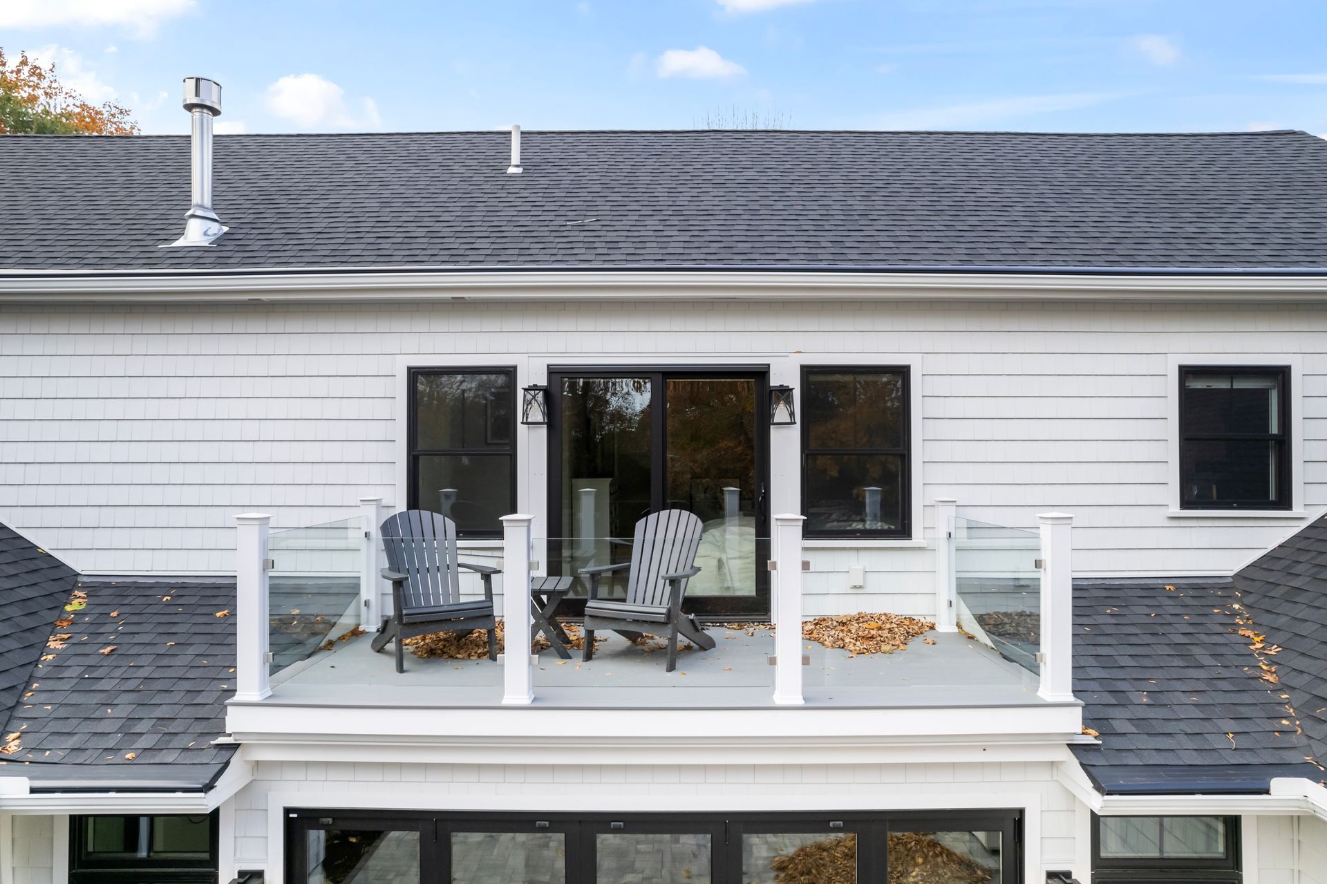Exterior of a white house with a balcony, two patio chairs, and a dark gray shingled roof