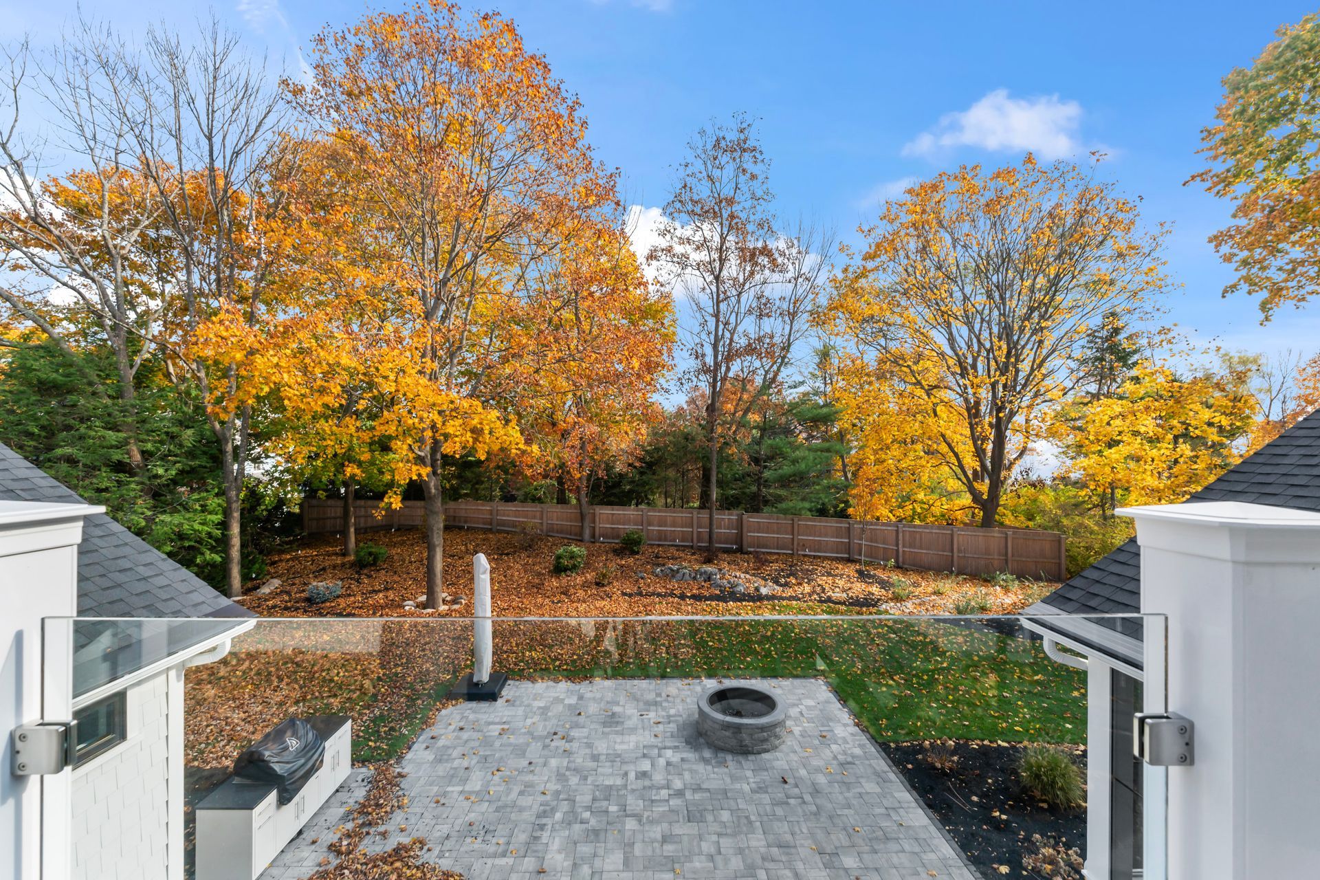 Backyard patio with fire pit, white railings, and autumn trees in orange and yellow foliage