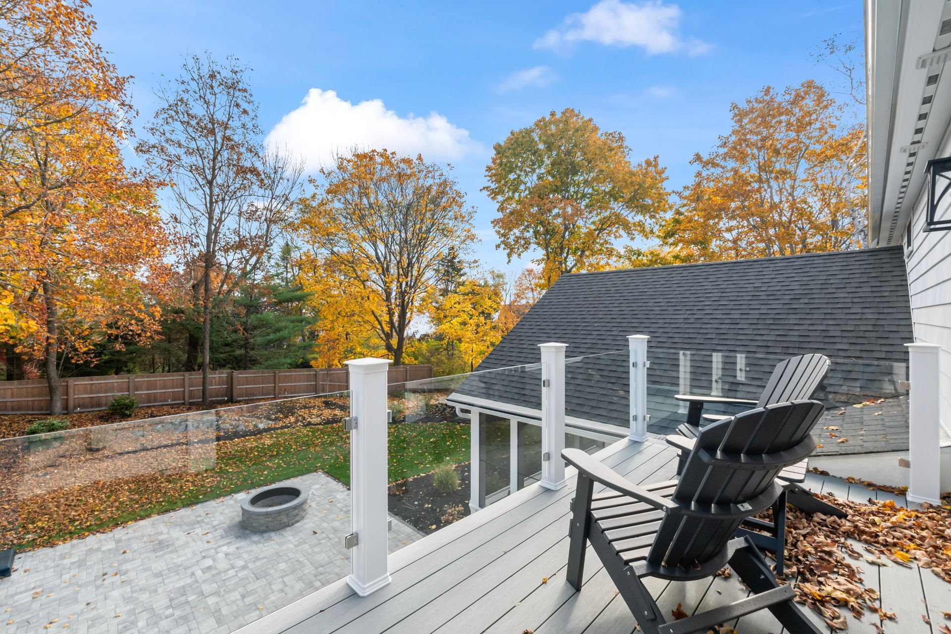 Deck with black chair overlooking autumn trees and a backyard fire pit under a blue sky
