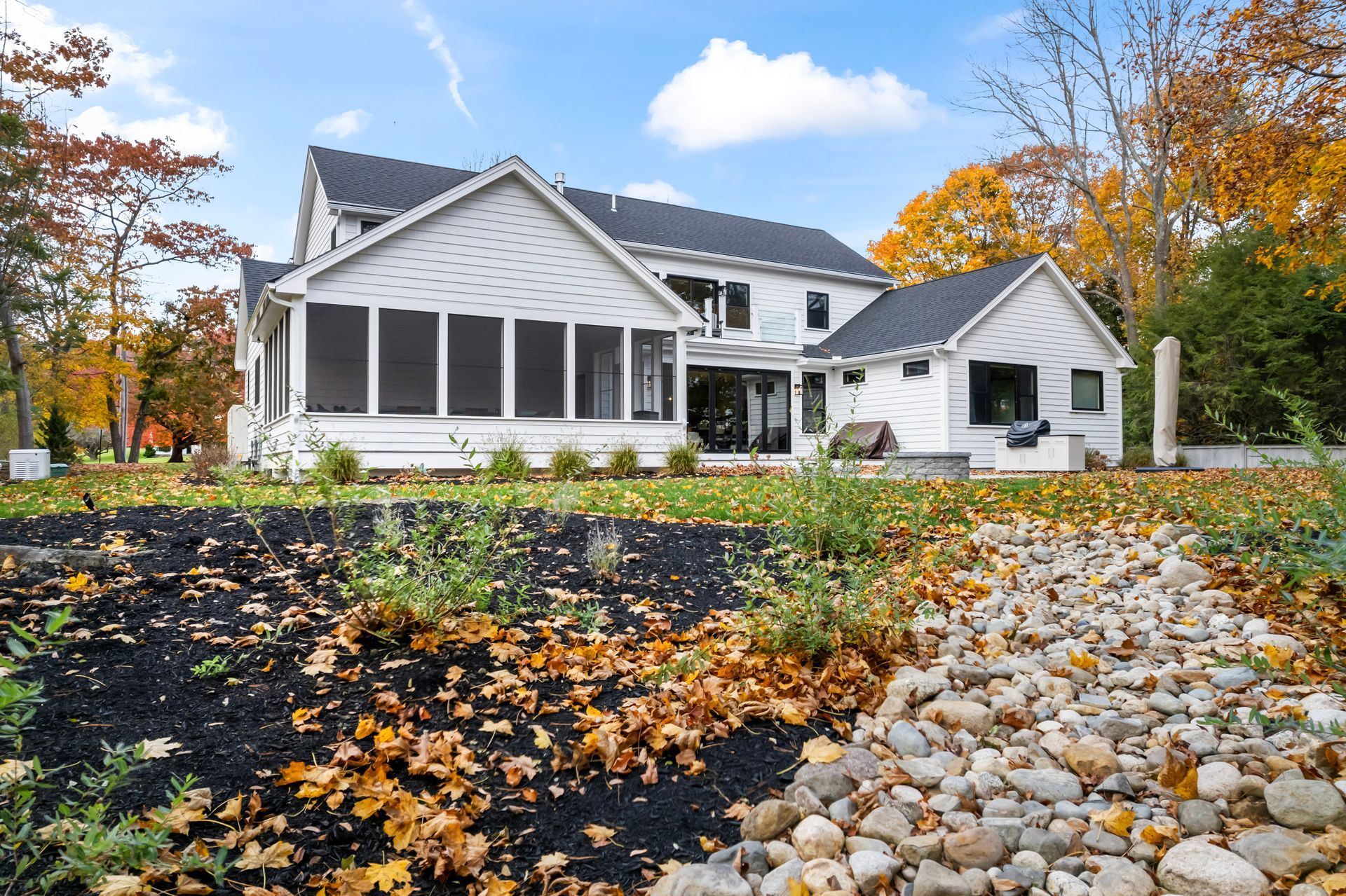 White house with screened porch and autumn trees beside a rocky gravel path