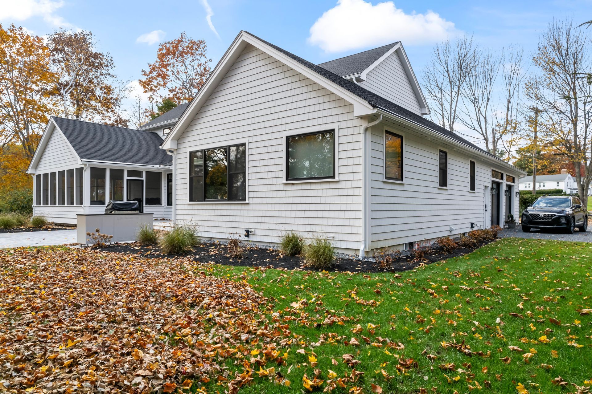 White house with black shutters and a screened porch, surrounded by autumn leaves and green lawn