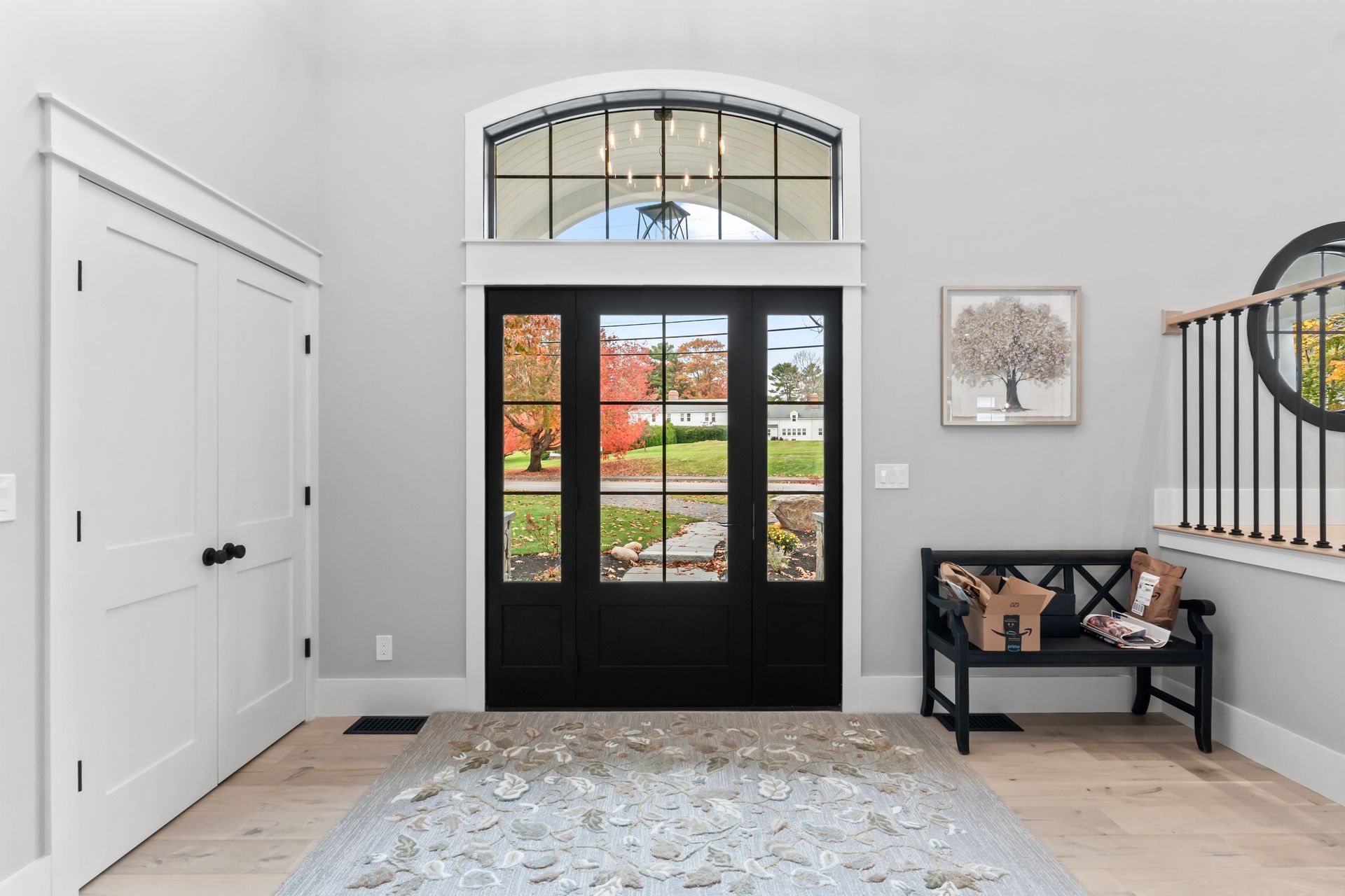 Bright entryway with black double doors, white walls, patterned rug, and a bench with pillows and wall art.