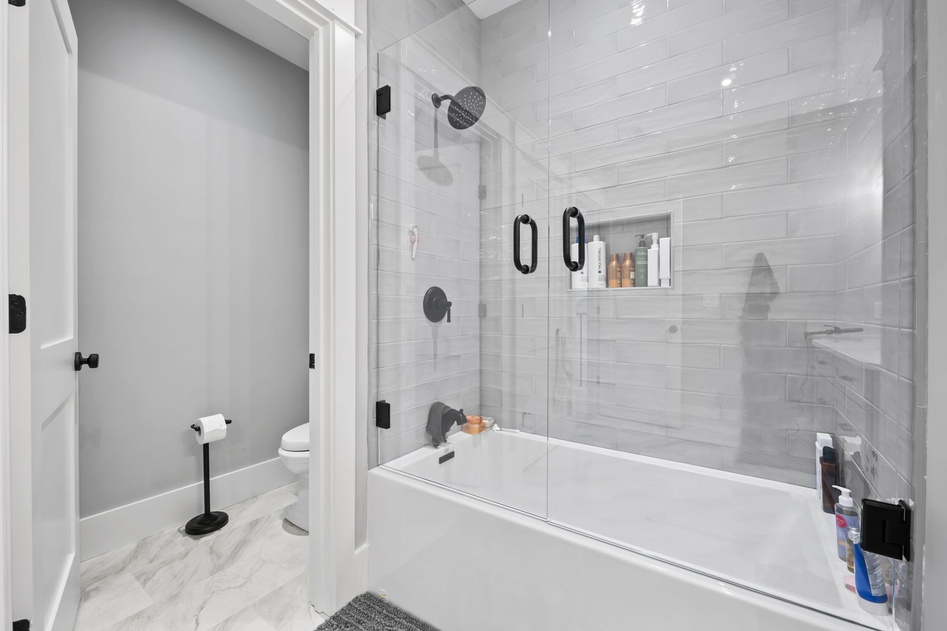 Modern white bathroom with tub-shower, gray tile floor, and a toilet in a separate alcove.