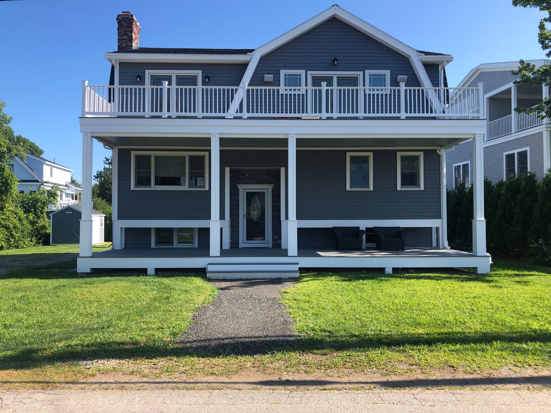 Blue two-story house with a front porch, white trim, and a front lawn under a clear sky