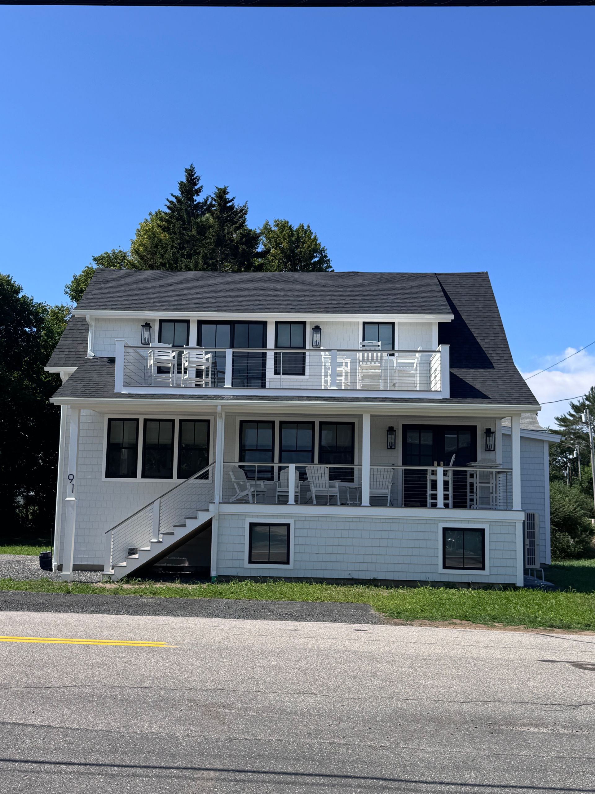 White two-story house with porch and balcony under a clear blue sky, viewed from the street