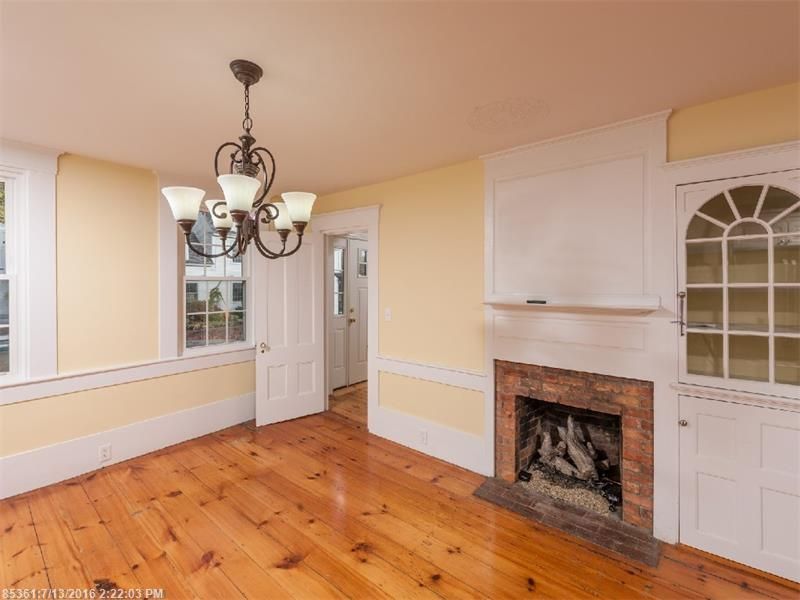 Empty dining room with hardwood floors, chandelier, fireplace, and built-in white cabinets.
