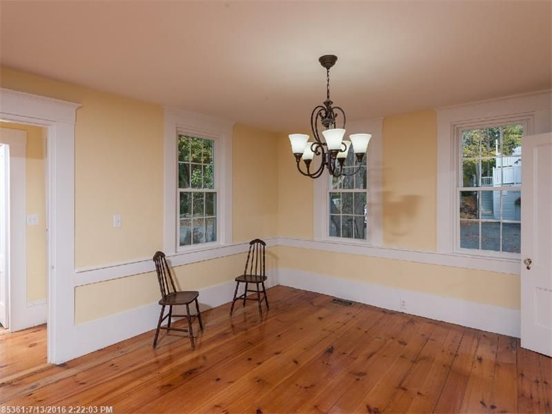 Empty dining room with hardwood floors, beige walls, two chairs, and a hanging chandelier