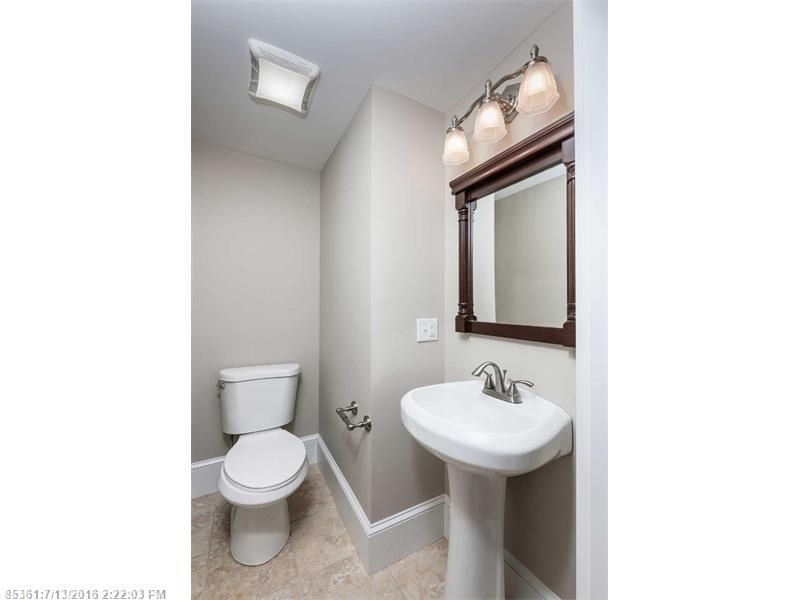 Small white bathroom with toilet, pedestal sink, mirror, and wall light in a narrow space