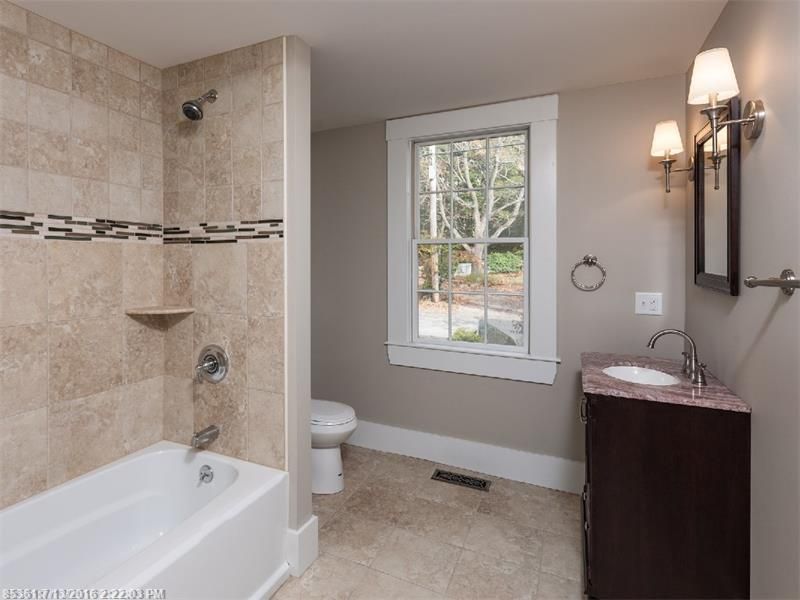 Modern bathroom with tiled shower, bathtub, window, and dark wood vanity sink.