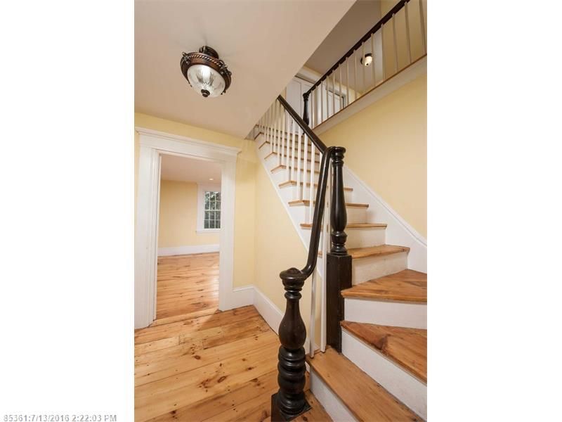 Bright foyer with wooden stairs, white walls, and hardwood floors leading to an adjacent room.