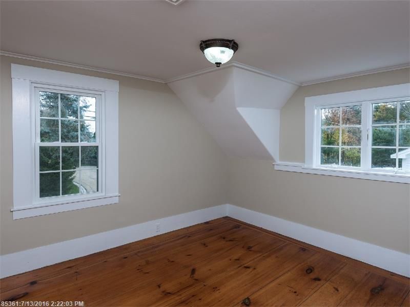 Empty room with white walls, hardwood floor, and two windows on adjacent walls.