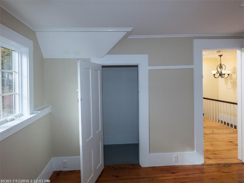 Empty beige room with open door, gray closet, window, and hardwood floor leading to hallway