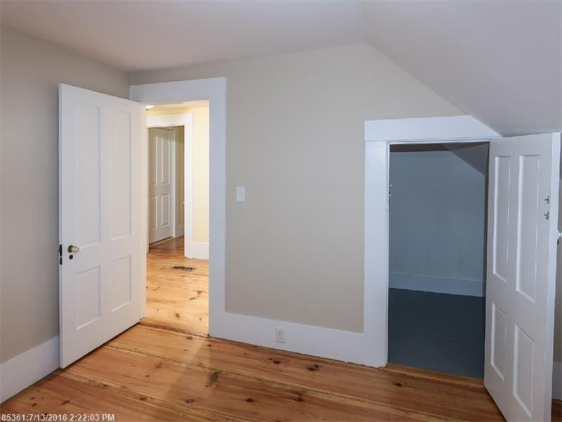 Empty white bedroom with hardwood floors and open doors to a hallway and closet