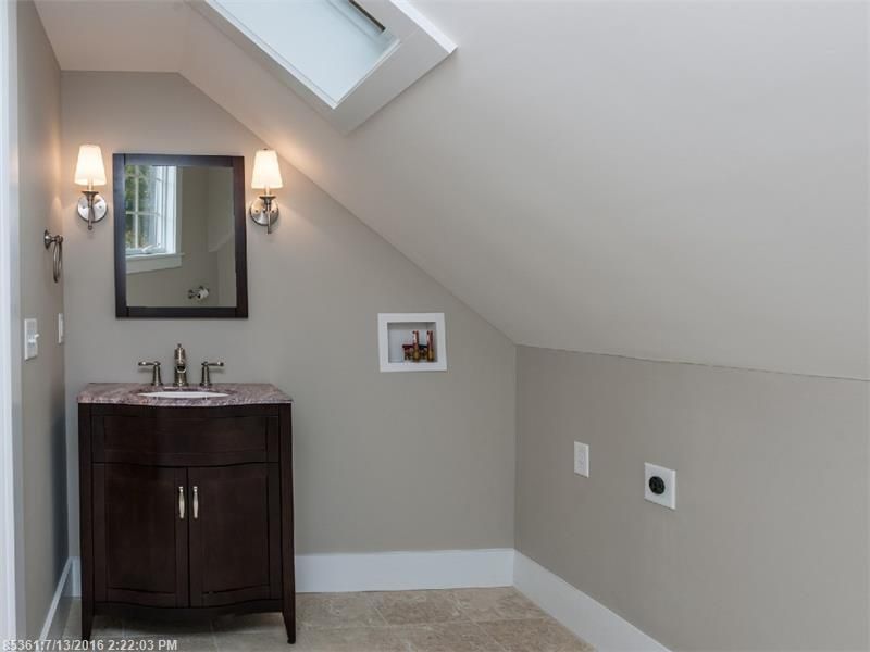 Small bathroom vanity with mirror and wall sconces in a sloped-ceiling attic room