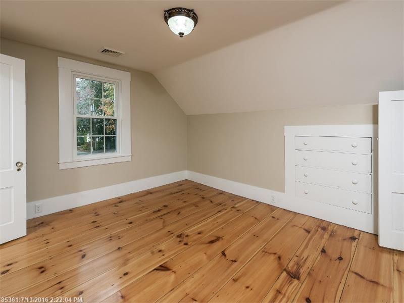 Empty attic-style bedroom with wood floors, sloped ceiling, window, and white dresser drawers