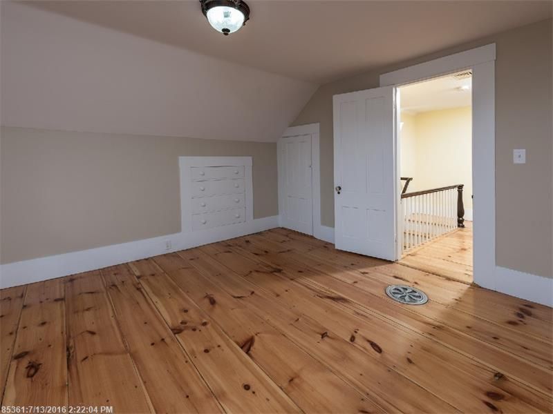 Empty bedroom with wood floors, beige walls, white trim, and an open door to a hallway.