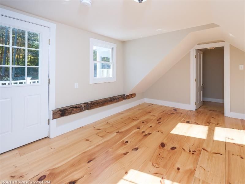Empty bright room with white walls, pine wood floor, door, window, and staircase opening