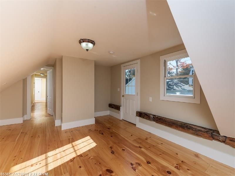 Empty sunlit attic room with sloped ceiling, hardwood floors, and two windows