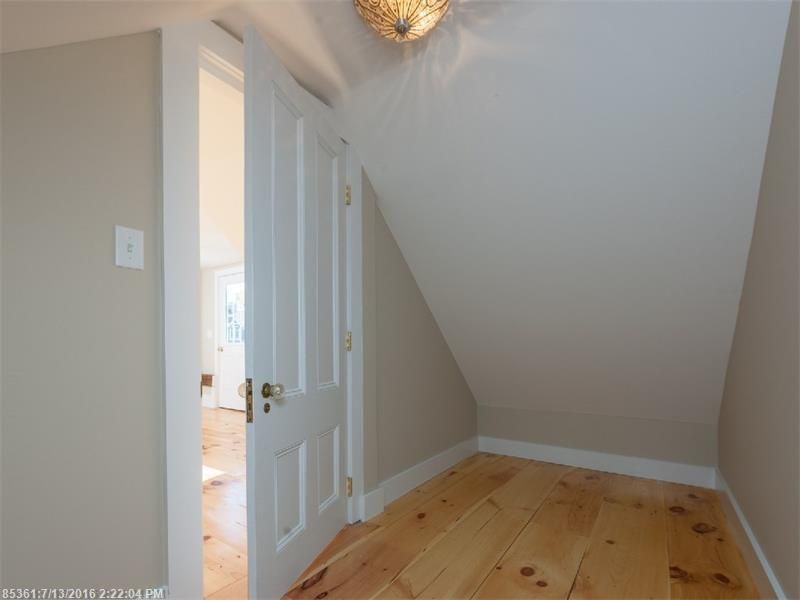 Empty attic room with sloped ceiling, white door, and light wood floor.