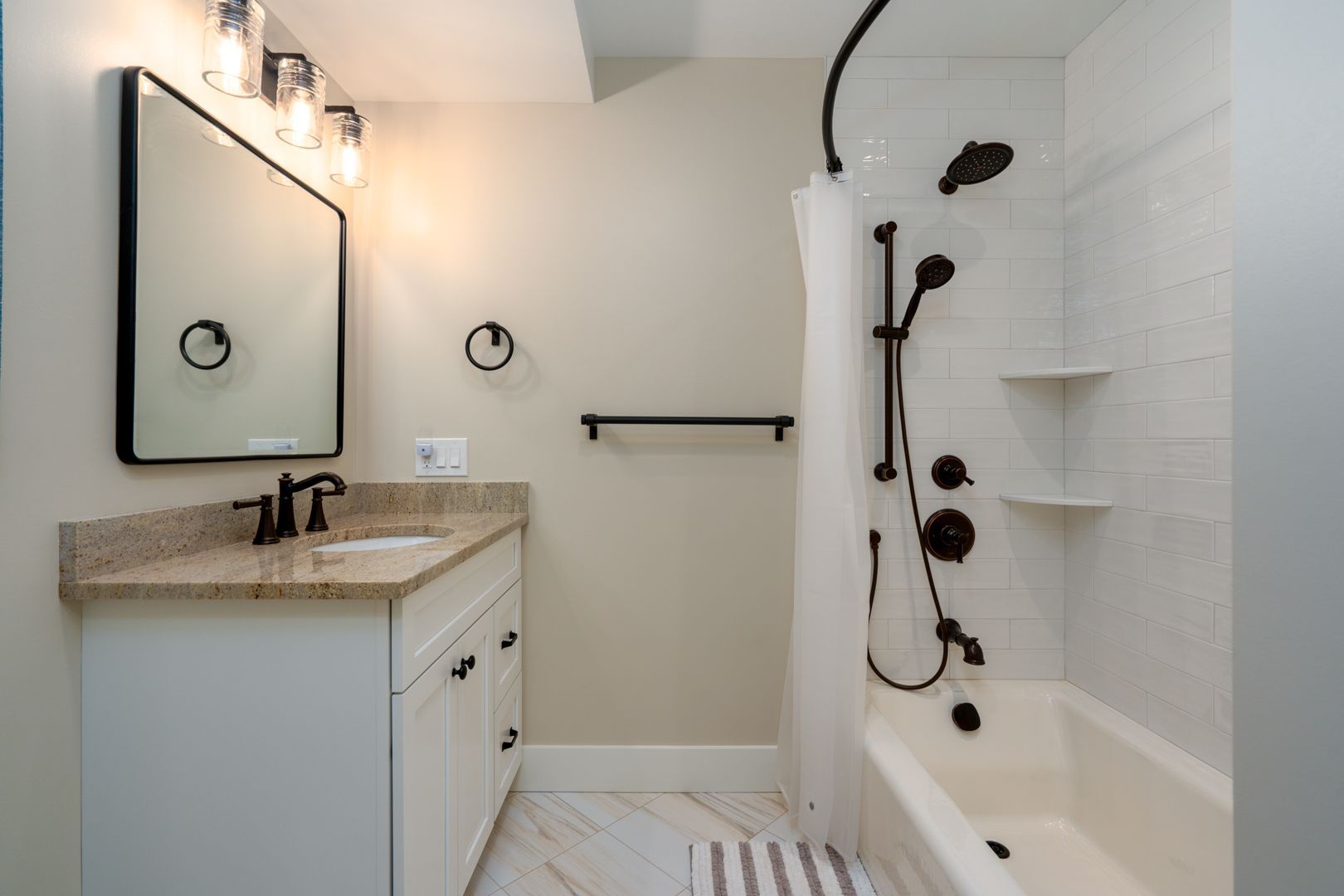 Bright bathroom with vanity, mirror lights, and a white shower with black fixtures.