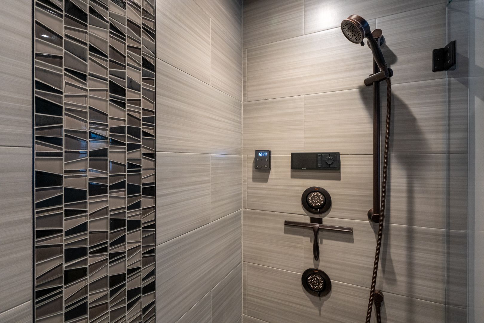 Modern tiled shower with handheld showerhead, controls, and a mosaic accent wall.