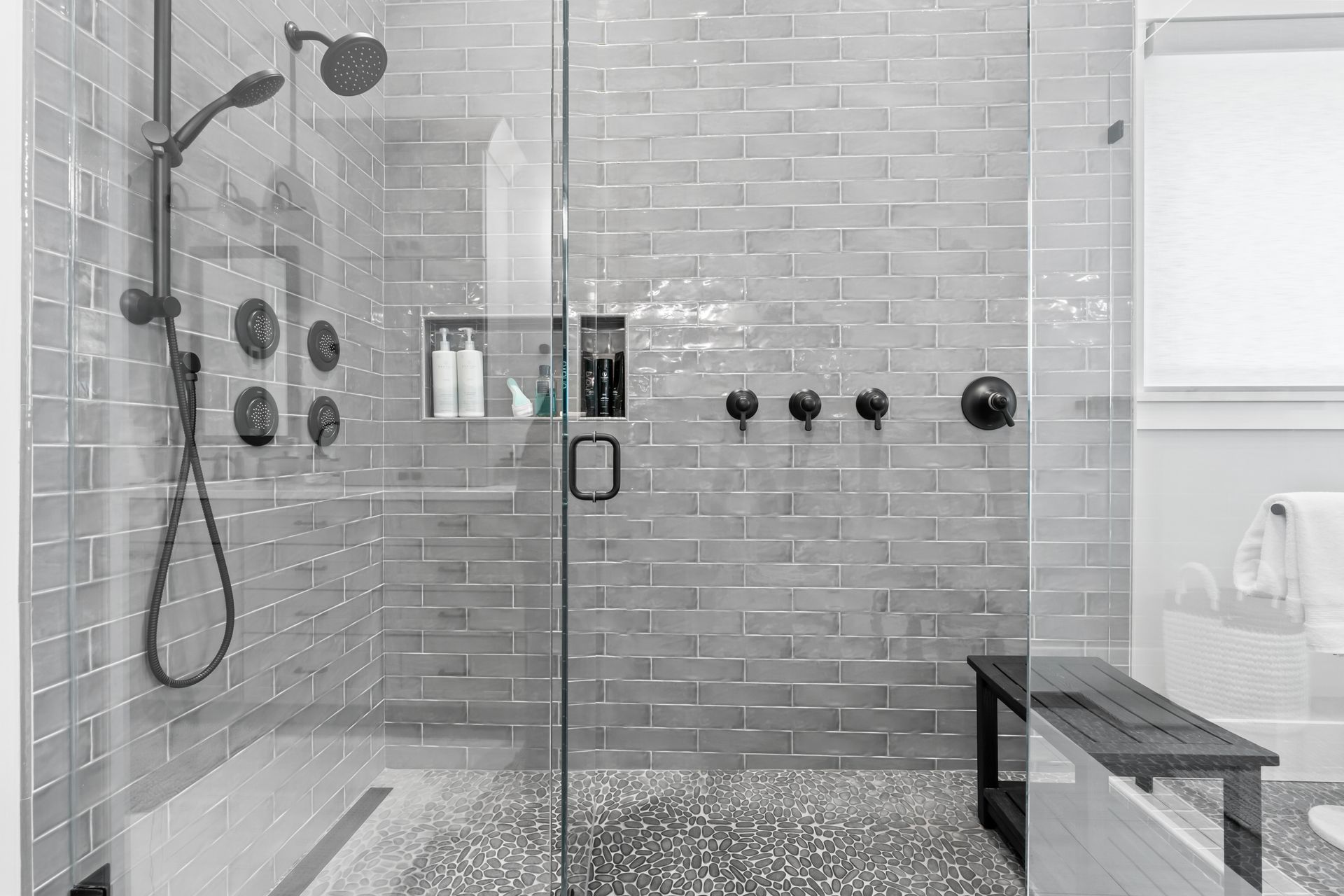 Modern gray tiled walk-in shower with glass door, rainfall showerhead, and built-in bench