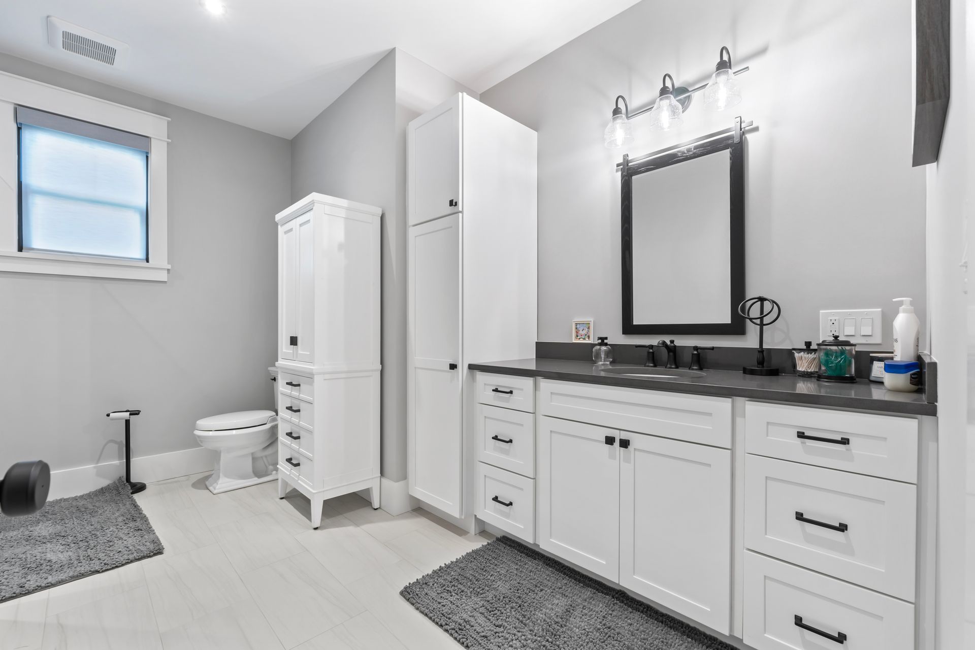 Modern bathroom with white vanity, black countertop, mirror, toilet, and storage cabinet